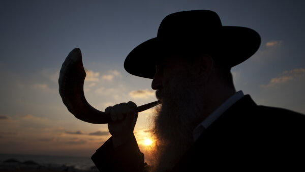 The silhouette of a man blowing a shofar, or ram's horn. Behind him is the sun setting.