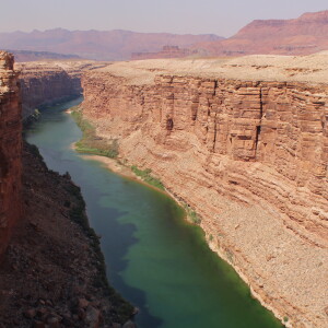 A wide bluish-green river flows through a desert canyon made of red rock