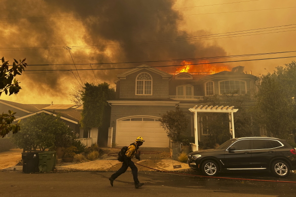 A residence burns as a firefighter battles the Palisades Fire in the Pacific Palisades neighborhood of Los Angeles Tuesday, Jan. 7, 2025. (AP Photo/Eugene Garcia)