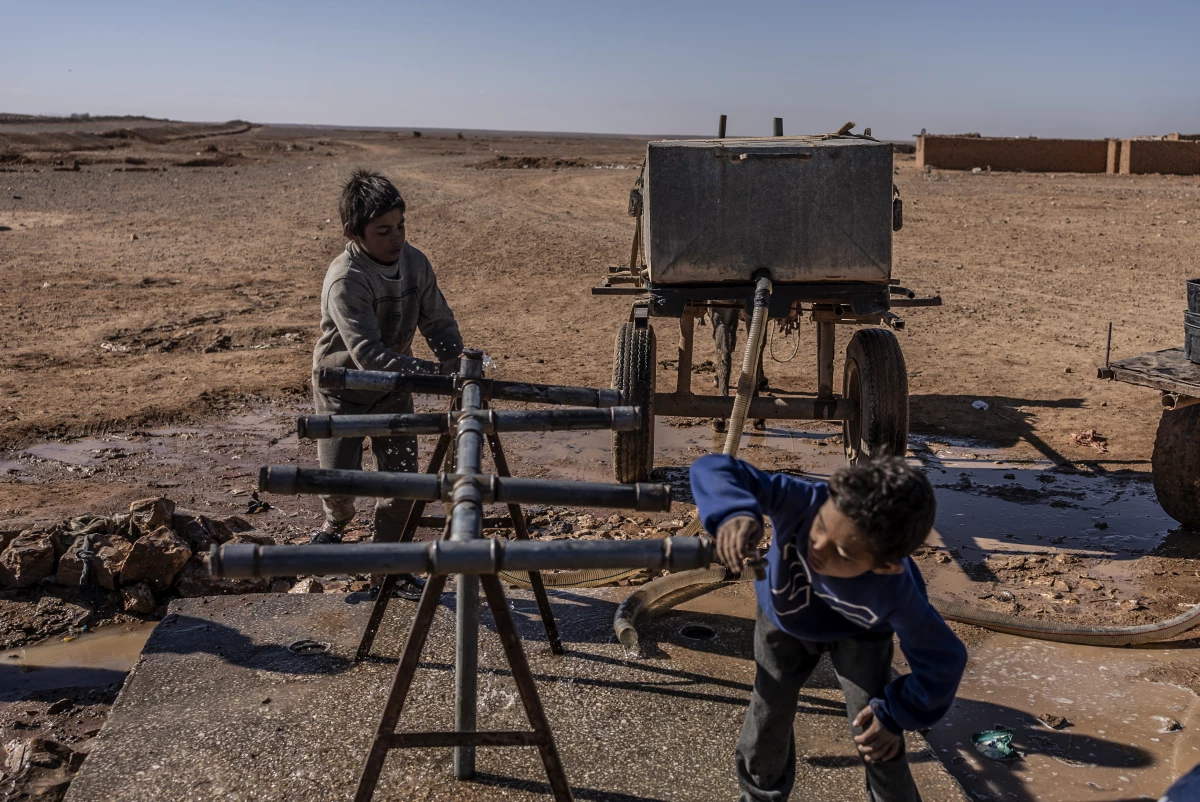 A child drinks water while another fills water in a jerry can on a cart pulled by a donkey at one of the fountains located on the edge of Rukban camp, near the southern Syrian border, Dec. 14.