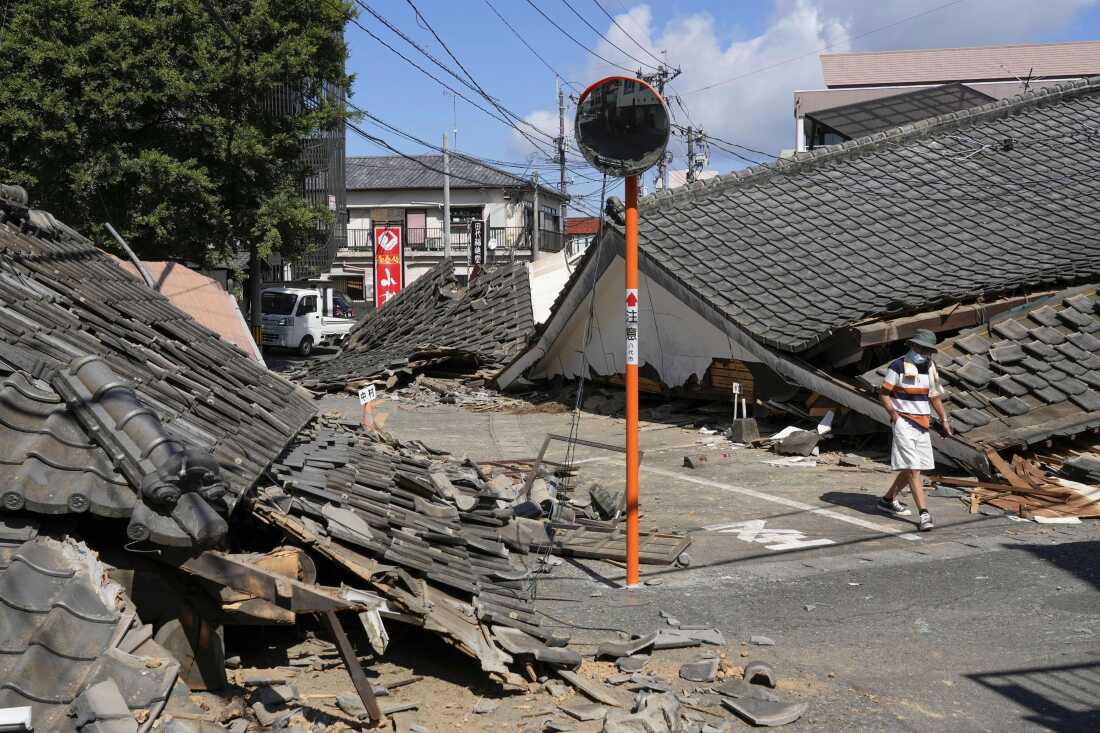 A person walks past the houses collapsed in an earthquake in Yatsushiro, Kumamoto Prefecture, southern Japan, Friday, July 31, 2026.