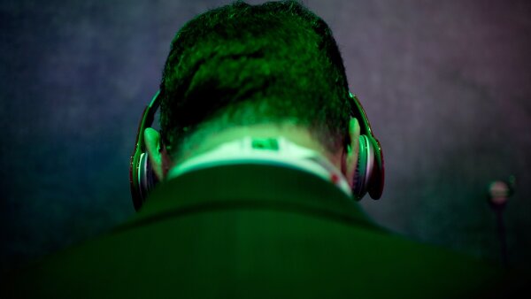 The back of a man's head, seen from the shoulders up. The man is wearing headphones, and he's lit by a green light.