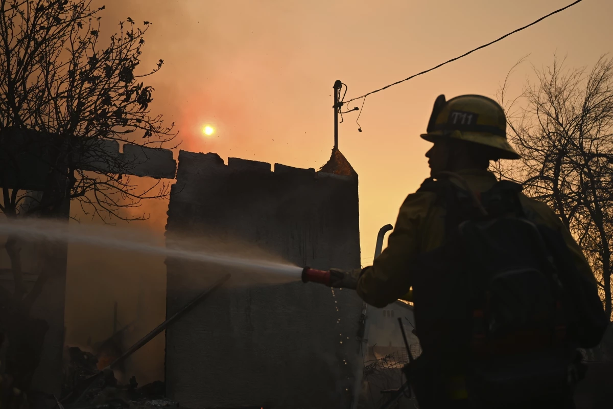 A firefighter waters down a home after the Eaton Fire burns in Altadena, Calif., Thursday, Jan. 9, 2025.