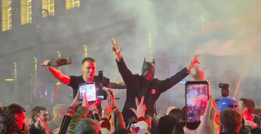 Crowds of people celebrate in the streets of Belgrade, Serbia, on Sunday night following the country's parliamentary election results. People are holding up their hands in celebration, and some people are holding up their smartphones to record the events.