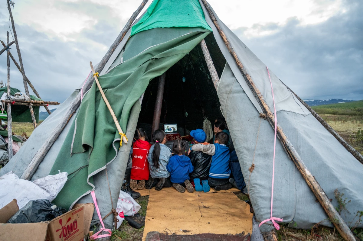 Children gather inside a traditional tent, known as an ortz, in the Siberian taiga of northern Mongolia, watching a documentary about a Norwegian reindeer herder who was visiting to learn about the lifestyle of the region's nomadic Dukha reindeer herders. Despite the community's remote location deep in the forest — accessible only by horseback or reindeer — families stay connected with the outside world with solar panels, car batteries and the occasional wi-fi connection.