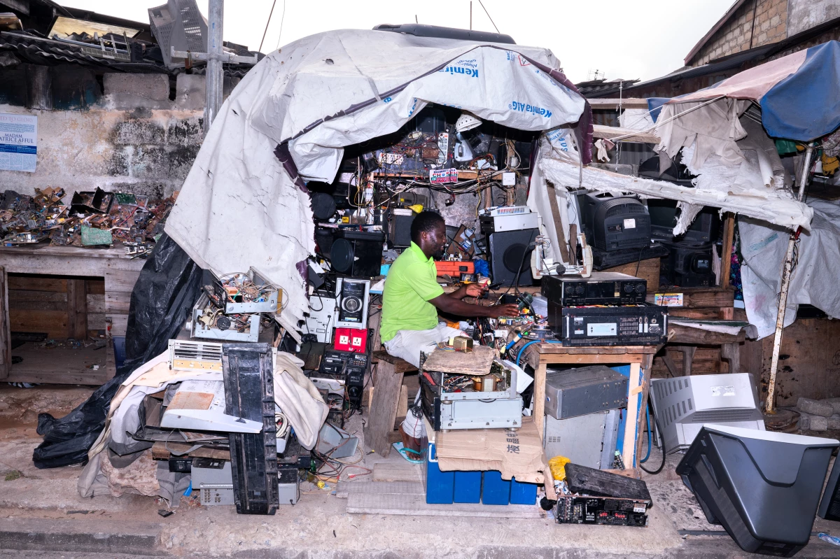 The man in the bright green shirt is working in one of the hundreds of small shops that have popped up around e-waste sites, where discarded items are repaired and resold, or broken down for parts.