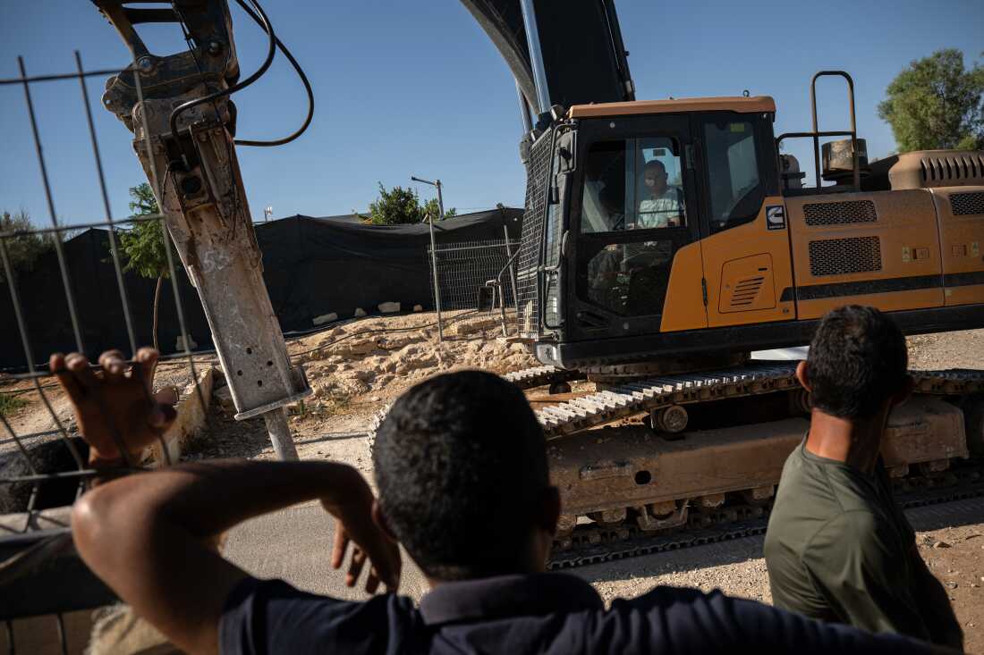 Palestinians mourning the killing of activist Awdah Hathaleen watch as the same excavator involved in the confrontation that led to his death drives through the village of Umm al-Kheir in the West Bank, returning to the Carmel settlement after working on a construction project beside the village, on August 4, 2025.