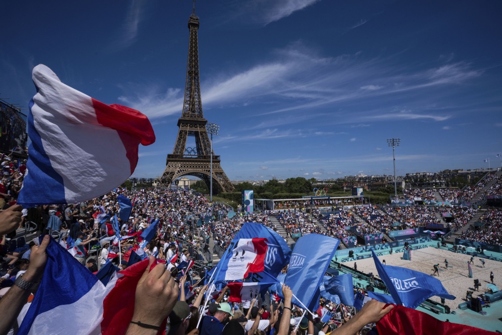 Supporters for Team France wave flags during the women's Pool C beach volleyball match between Germany and France at the Eiffel Tower Stadium on Sunday. (AP)