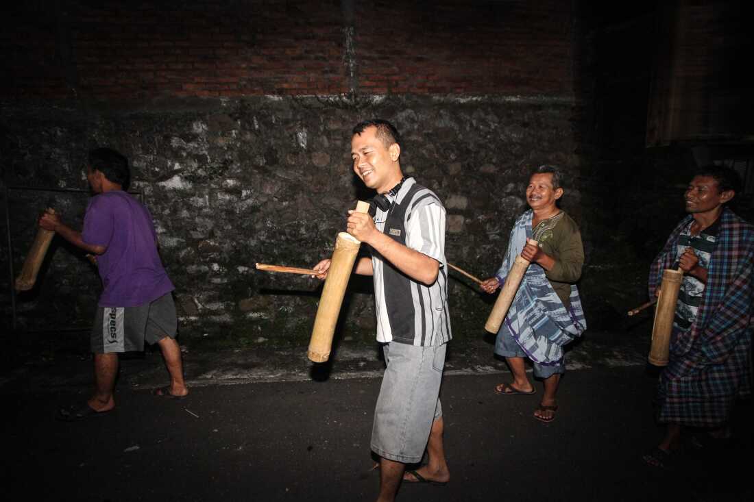 暗闇の中を歩くインドネシアのムスリム男性4人が、杖を使って伝統的な木製ドラムの「ケントンガン」を叩き、ラマダン期間中の早朝の断食前の食事であるサフルのために人々を起こしている様子を捉えた写真。2014年7月3日、ジャワ島中部セマラン。
