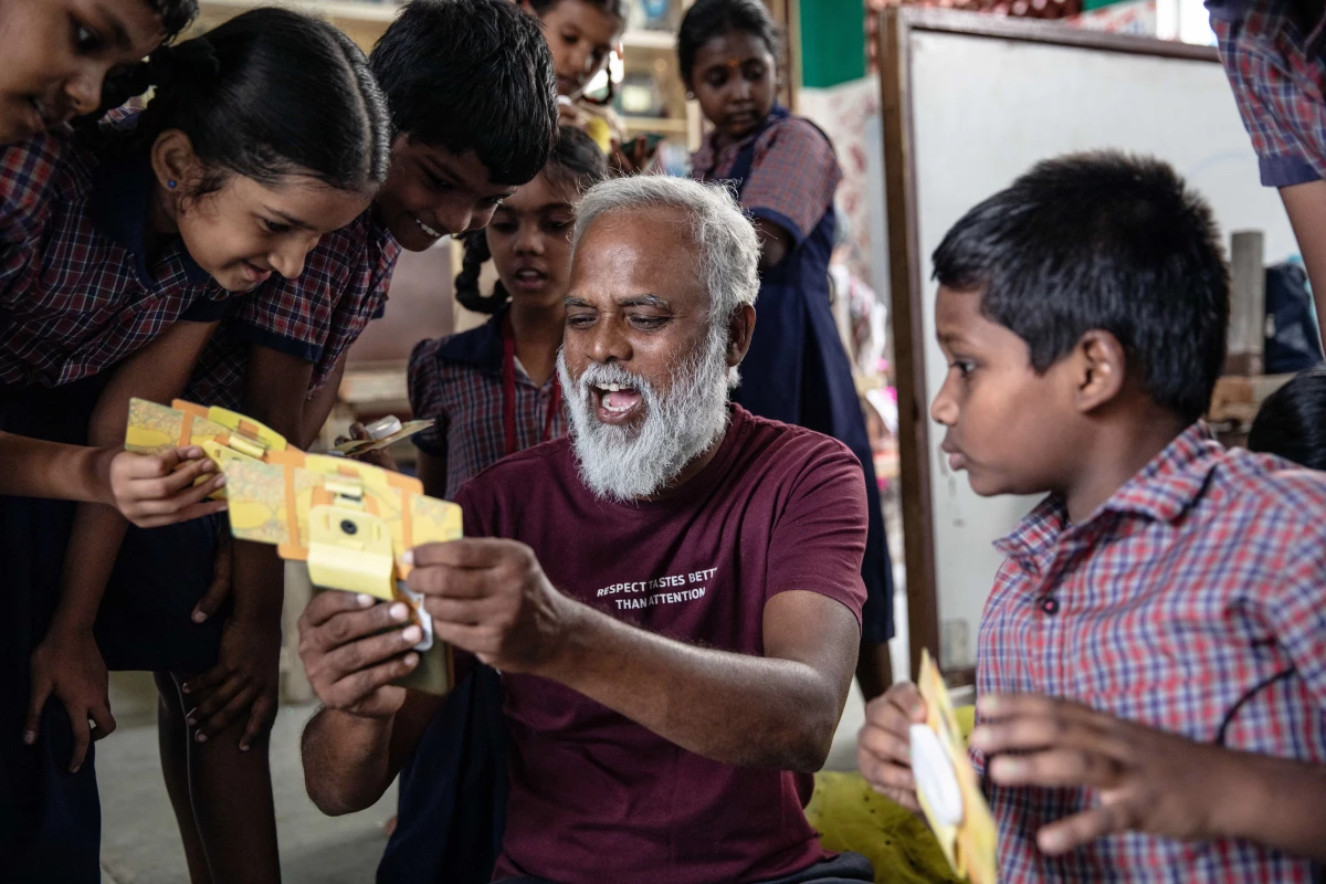 Mo Pandiarajan, founder of Eden school, shows students a view of a specimen in a Foldscope, which he's attached to his mobile phone.