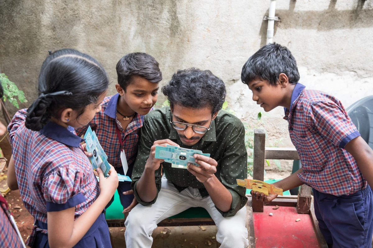A.Santhos inserts a slide into the foldscope. He is a former student who lives in the neigbourhood and keeps in touch with the students of his alma mater, often taking them for nature walks to examine the world around them through the foldscope.