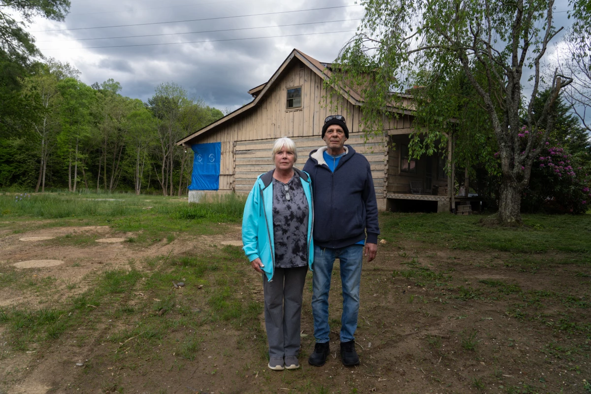 Stuart and Jackie Pacheo stand where the entryway to their home of 30 years was before the floods from Hurricane Helene washed it away. The circles of the tops of foundation pillars in the dirt behind them are all that remain of the Pacheo home.