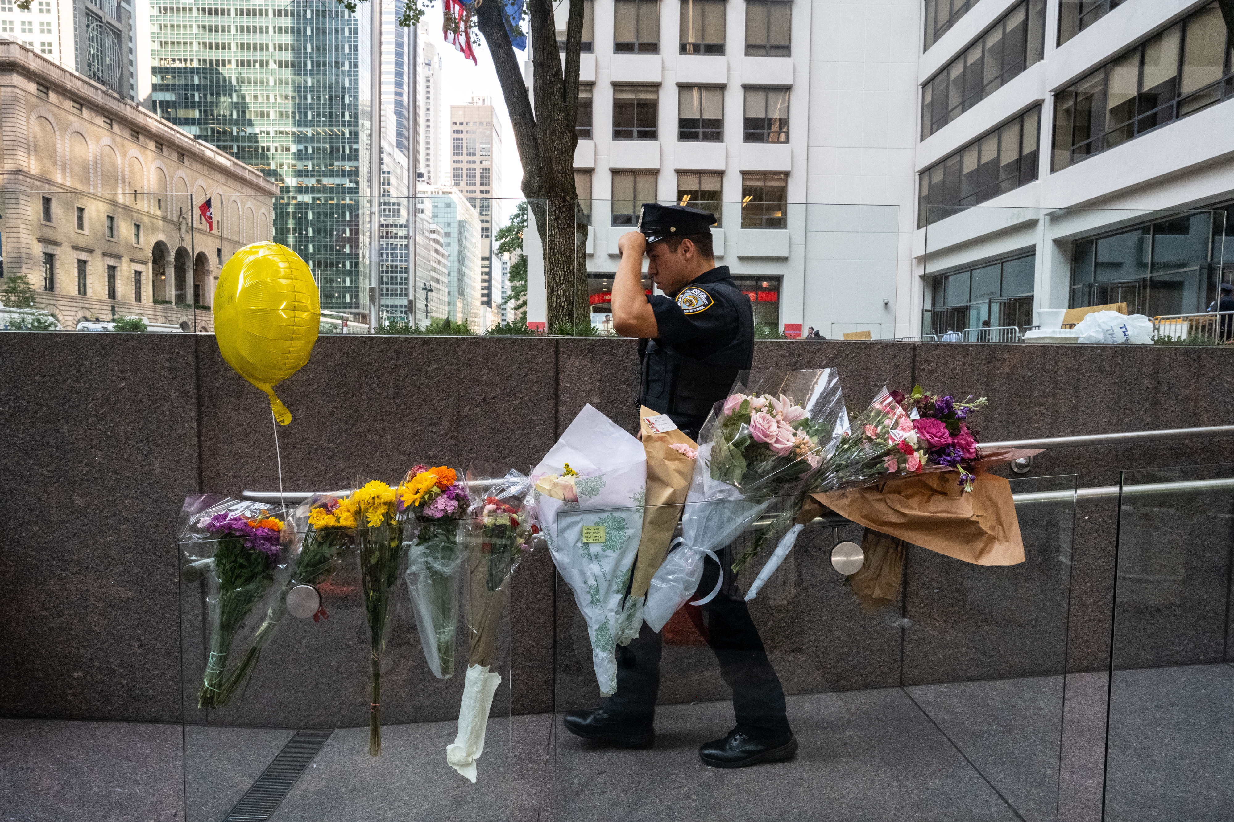 A New York City police officer walks past flowers placed outside the midtown office building where a gunman killed four people on July 29, 2025 in New York City.