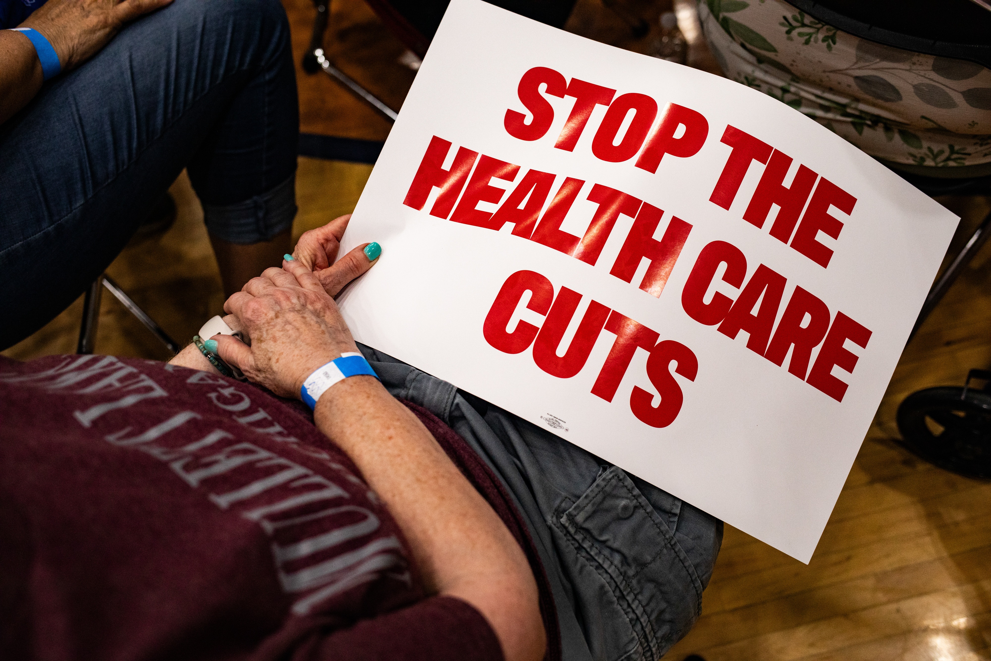 An attendee holds a "Stop The Health Care Cuts" sign on June 6 at a Democratic town hall in Lansing, Mich. In July, Congressional Democrats failed to stop Republicans from passing a tax-and-spending bill that requires 40 states and D.C. to institute Medicaid work requirements.