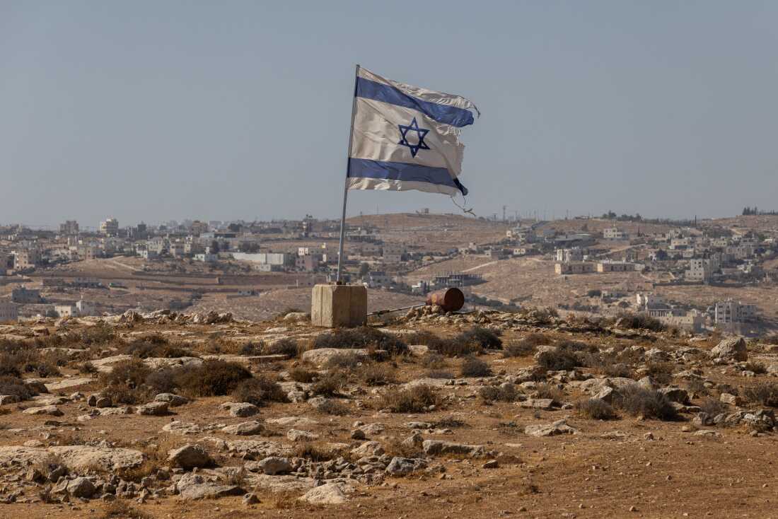 An Israeli flag flies along a highway near the settlement of Carmel on Aug. 4, 2025 in the South Hebron Hills of the West Bank. The region has seen an increase in violence against Palestinians in recent days, with what the United Nations Human Rights Office (OHCHR) condemns as a "pattern of the use of unnecessary and disproportionate force that resulted in the unlawful killing and injury of Palestinians," following multiple incidents involving Israeli settlers and security forces in the West Bank.