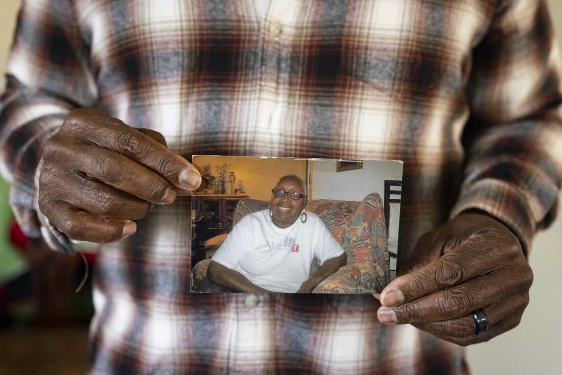 A close-up photo shows Leslie Adams' hands holding a snapshot of his mother. She is smiling broadly.