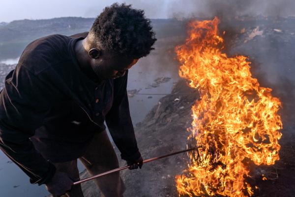 Old Fadama, Accra, Ghana, February 9, 2023. Simon Aniah, 24, burns scrap electrical cables to recover copper by the Korle Lagoon. From Vea, northeastern Ghana, Simon and hundreds of other young people migrate from his village and other areas in the Upper East to Accra to engage in e-waste work as a means to achieve upward social mobility. Upper East, the region Simon comes from, has the highest unemployment rate among the population 15-24 years in Ghana (2021 Ghana Census).