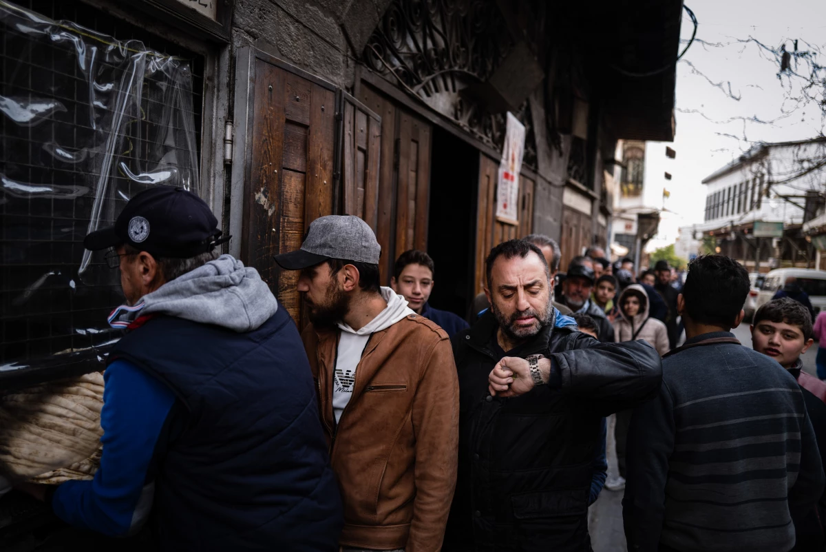 A Syrian man checks his watch while waiting at a breadline at a bakery in the Syrian capital Damascus.
