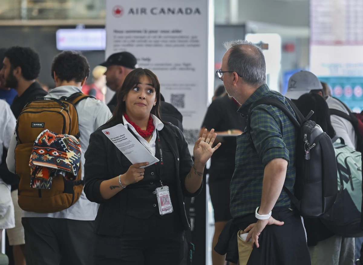 An Air Canada agent, left, talks with a man as Air Canada flight attendants strike at Montreal-Pierre Elliott Trudeau International Airport in Montreal, Saturday, Aug. 16, 2025.