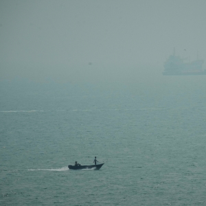 A motorboat travels past commercial vessels anchored amid haze in the Strait of Hormuz off Bandar Abbas, Iran, Monday, Sept. 7, 2026.