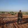 With his back to the camera, a senior Uyghur militant in camouflage-print pants stands facing an olive grove in northern Syria.