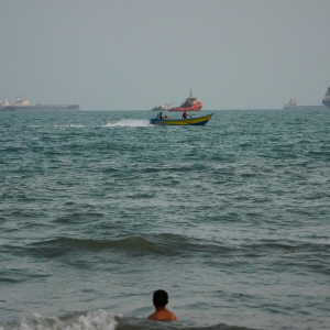 A swimmer remains near the shore as a motorboat passes commercial vessels anchored in the Strait of Hormuz off Bandar Abbas, Iran,on Friday.