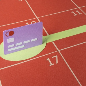 An illustration made of cut paper shows a purple credit card standing up on a flat, red calendar with dates numbered in the grid. A green circle below the card turns into a line that stretches out into the future, demonstrating making a plan to pay off credit card debt.