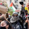 This photo shows a crowd of students taking part in pro-Palestinian protests in November. Some are wearing keffiyehs. Some are holding signs. The student in the middle is holding a fist in the air.