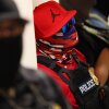Federal agents wearing masks patrol the halls of the immigration court at the Ted Weiss Federal Building in New York City on July 9. The agent in the center of the photo is wearing a red baseball cap with the Air Jordan logo on it, sunglasses with blue lenses, a red and blue bandana that covers the face, a red shirt and a black vest that says "POLICE" on the front.