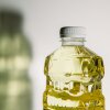 Una fotografía cercana del aceite de canola en una botella de plástico. La sombra de la botella se vierte a la izquierda de la botella en la pared blanca detrás de la botella de aceite de semilla.