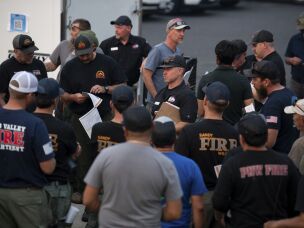 Support staff of the California Complex Incident Management Team 7 give briefings to firefighters as day crew and night crew switch on the evening of August 3, 2026 at Mt. Spokane High School in Mead, Wash.