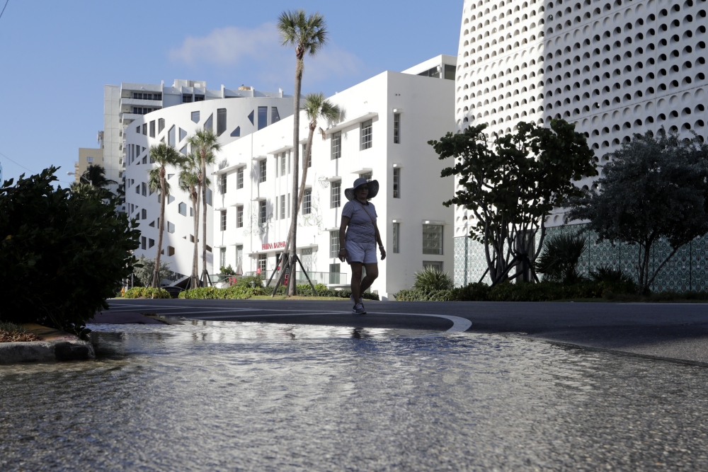 A woman walks along a flooded street caused by a king tide in Miami Beach, Fla., in 2019. So-called sunny day floods are getting more common in many coastal areas as seas rise due to human-caused climate change. (AP)