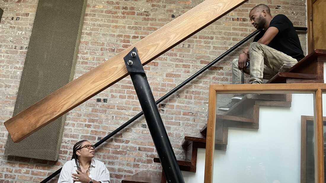 Michel Martin sits on a set of stairs and looks up at Trombone Shorty. 