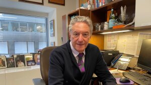 Dr. Steven Lamm sits at a desk in an office in front of a large window.