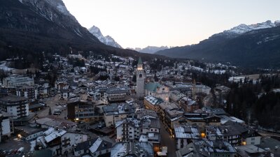The illuminated bell tower of the Basilica Minore dei Santi Filippo e Giacomo stands at the heart of Cortina d’Ampezzo as evening settles over the valley. 