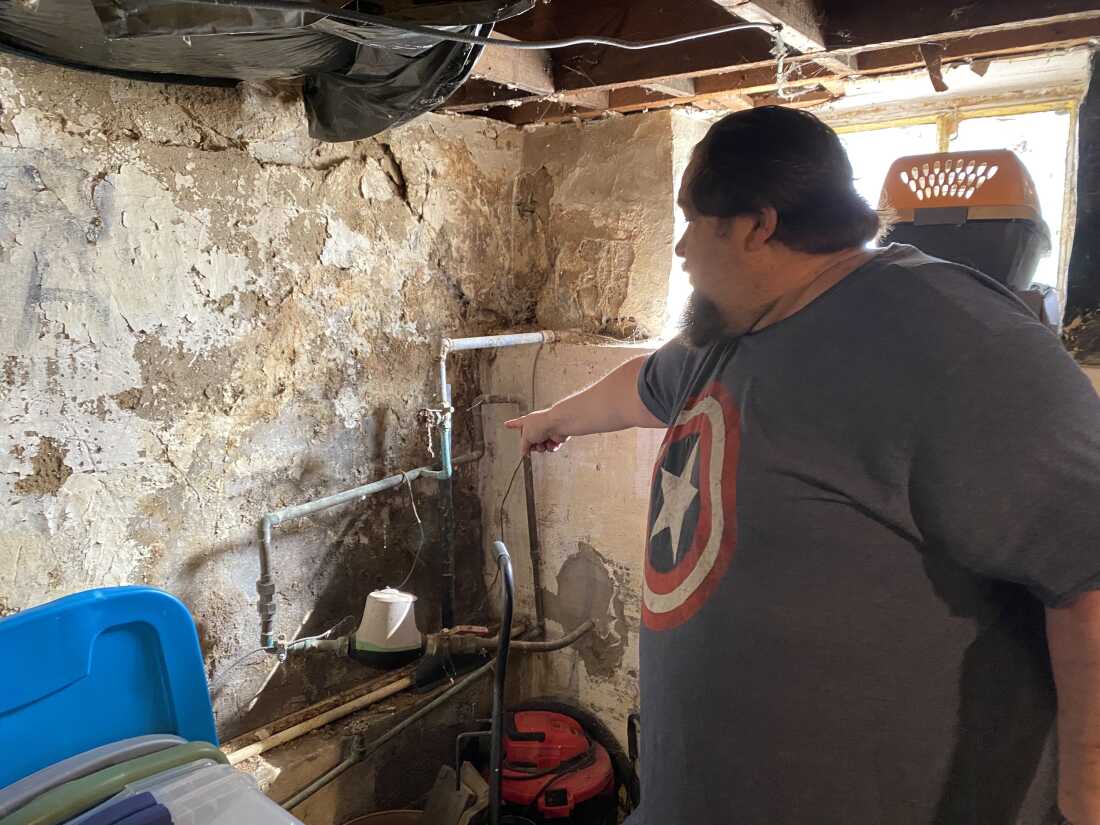 In his basement, Robert Cox points to the original foundation that's crumbling. The older home has no gutters, and rain also gushes down from a steep hill across the road.