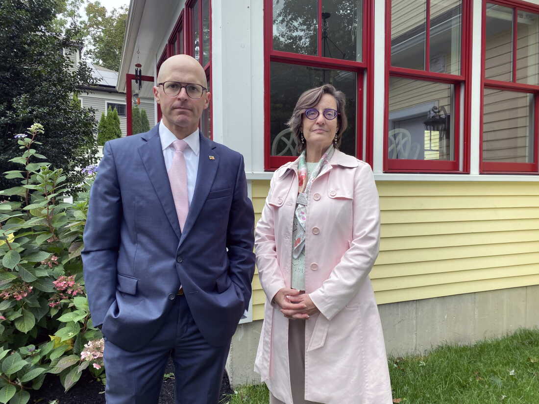 Adam Chapdelaine and Jill Hai stand in front of a house with yellow clapboard and windows framed in red.