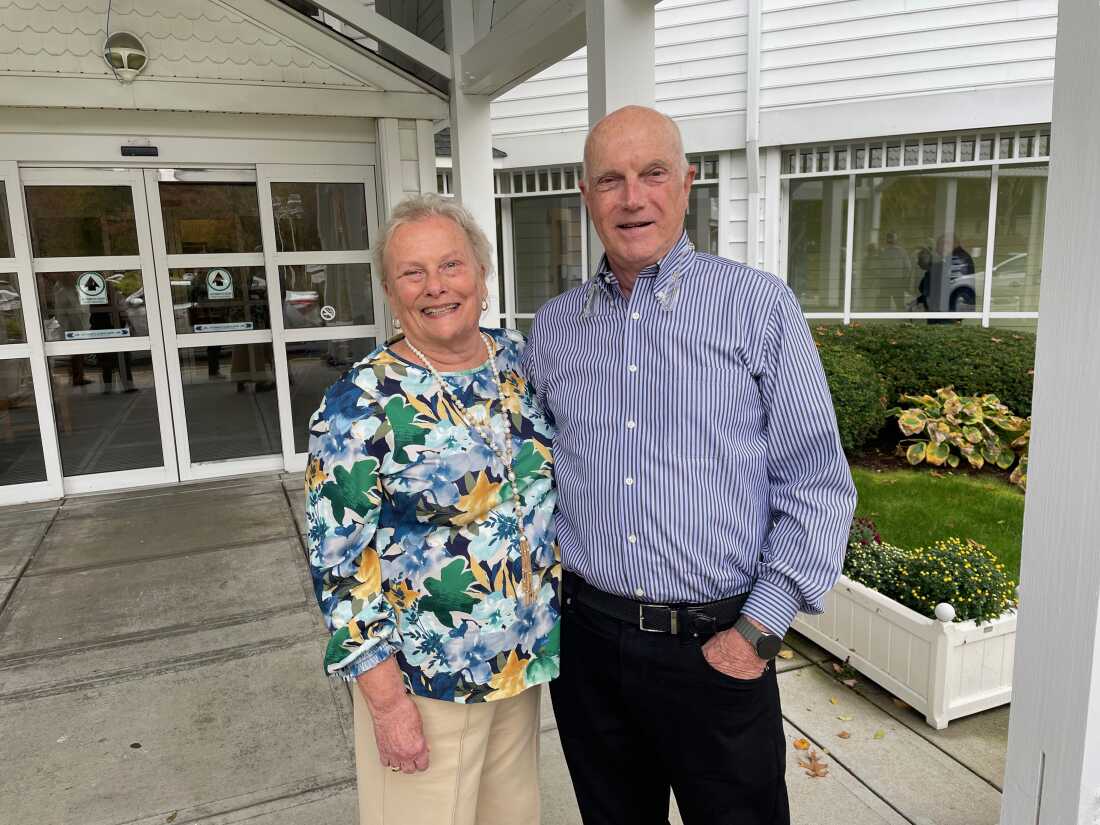 Helen and Whiting Houston are shown standing in front of members of their senior community; they both smile widely.