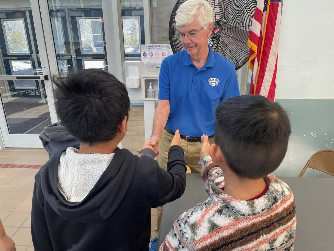 Three 4th grade boys all have their hands extended, waiting to shake hands with an older gentleman with white hair. 