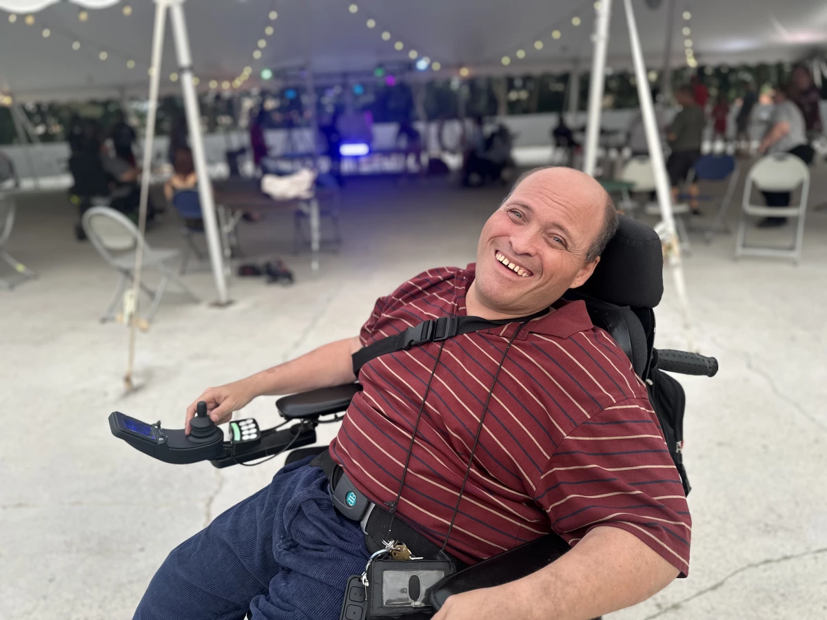 On the Skate Downtown roller rink, Michael Denlinger relaxes into his electric-powered wheelchair and flashes a smile with a white tent and party lights behind him.