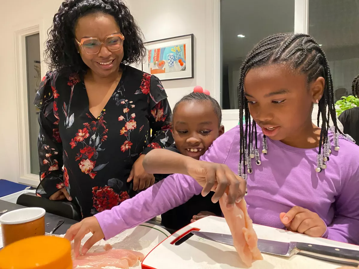 Ayesha Rascoe watches her daughters Annalise, 7, and Gabrielle, 8, prepare chicken. (left to right)