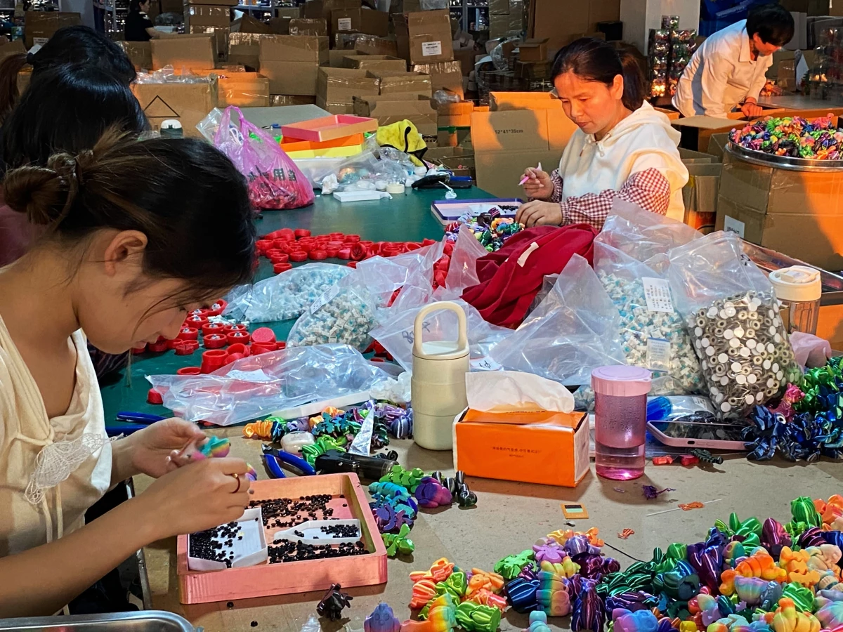 Workers decorate 3D-printed toys, including giving the plastic animals eyes.