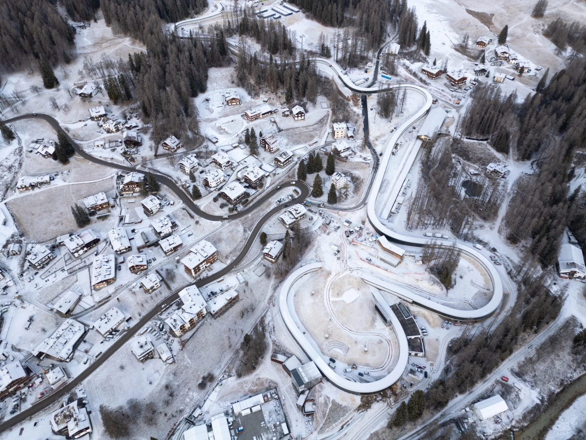 An overhead shot captures construction of the new Cortina Sliding Center, a track spanning just under a mile with 16 curves, designed to host bobsled, skeleton, and luge events for the Milano Cortina 2026 Winter Olympics.