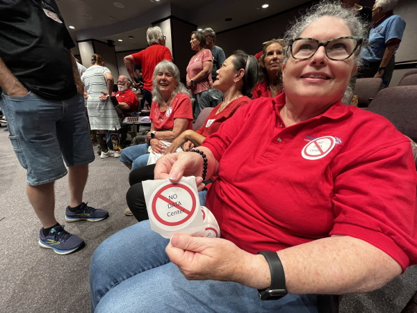 In this photo, Meg Lemaster holds a round white sticker that says "No Data Center" and has a red ring with a slash through it on top of the text. Attending a City Council meeting, she's seated with other opponents of the data center that was proposed for Chesapeake, Virginia.