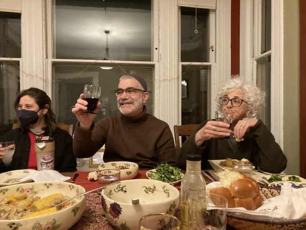 Three people raise their glasses while sitting at a table full of food.