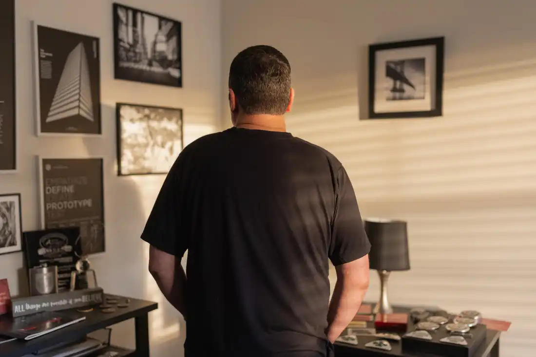 In this photo, Scott Boyd stands in a room in his house, with his back facing the camera. He's wearing a dark T-shirt.