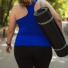 A woman is shown from the back. She's wearing workout clothes and is carrying a rolled-up exercise mat.