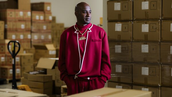  A man in a red hoodie stands among cardboard boxes.