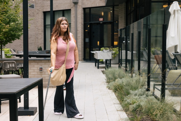 Christina Cooley, who requires a cane to walk and is on disability, walks through the courtyard of The Laureate, where rents typically range from about $1,335 for a smaller one-bedroom — far below the county median — to $3,885 for a larger two-bedroom.