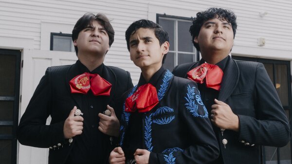 Antonio, Joshua, and Caleb Gámez-Cuéllar, wearing pristine black charro suits and big red bow ties, stand in front of Gruene Hall.